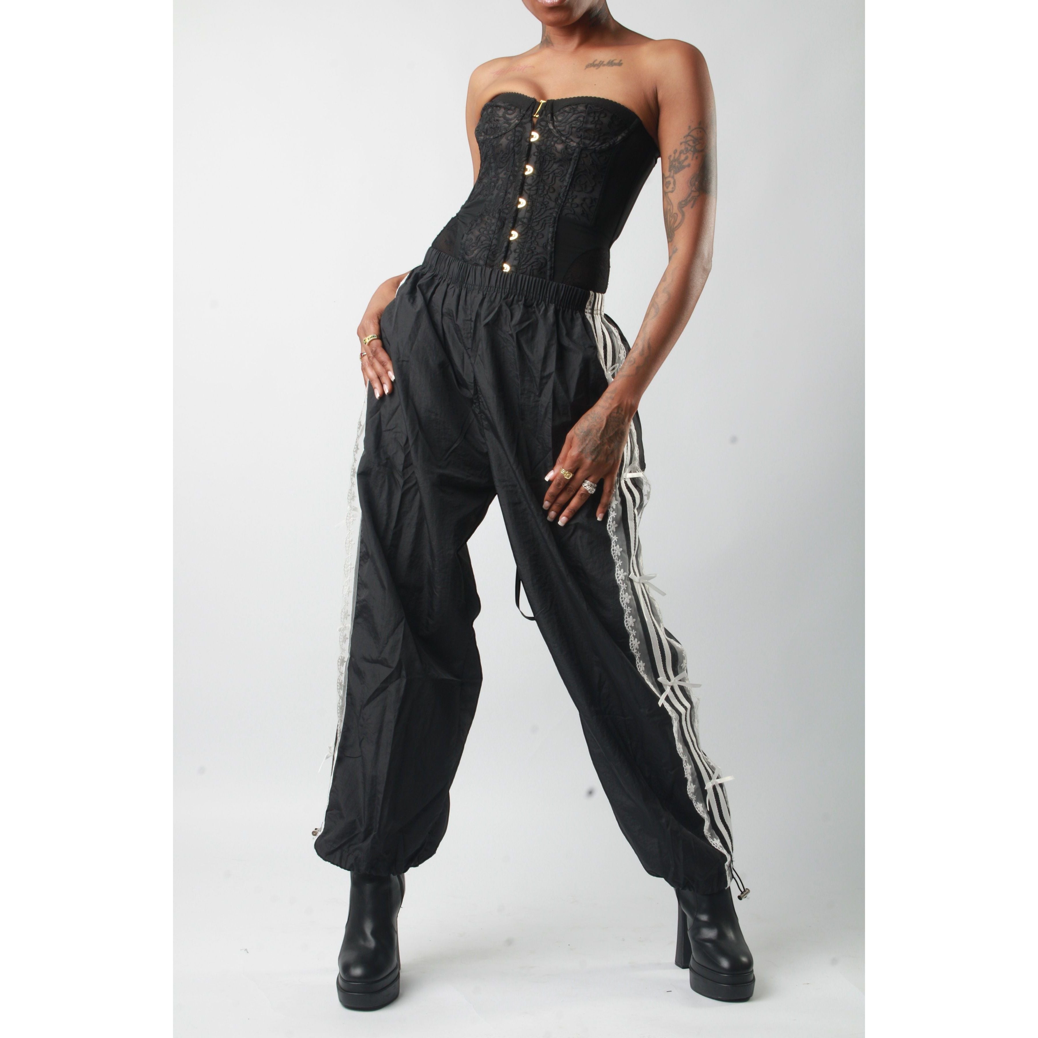 Sweet Plus Savage black track pants with white lace trim and adjustable ankle cuffs. Model is wearing a black corset top and platform boots.